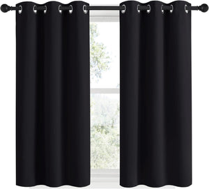 Pair of solid black blackout curtains with silver grommet tops, hanging on a black rod against a sunlit window.