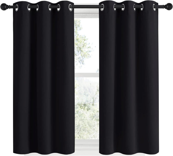 Pair of solid black blackout curtains with silver grommet tops, hanging on a black rod against a sunlit window.