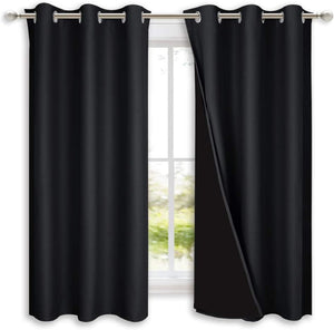 Black blackout curtains with silver grommet tops on a rod, one pulled back showing opaque lining.