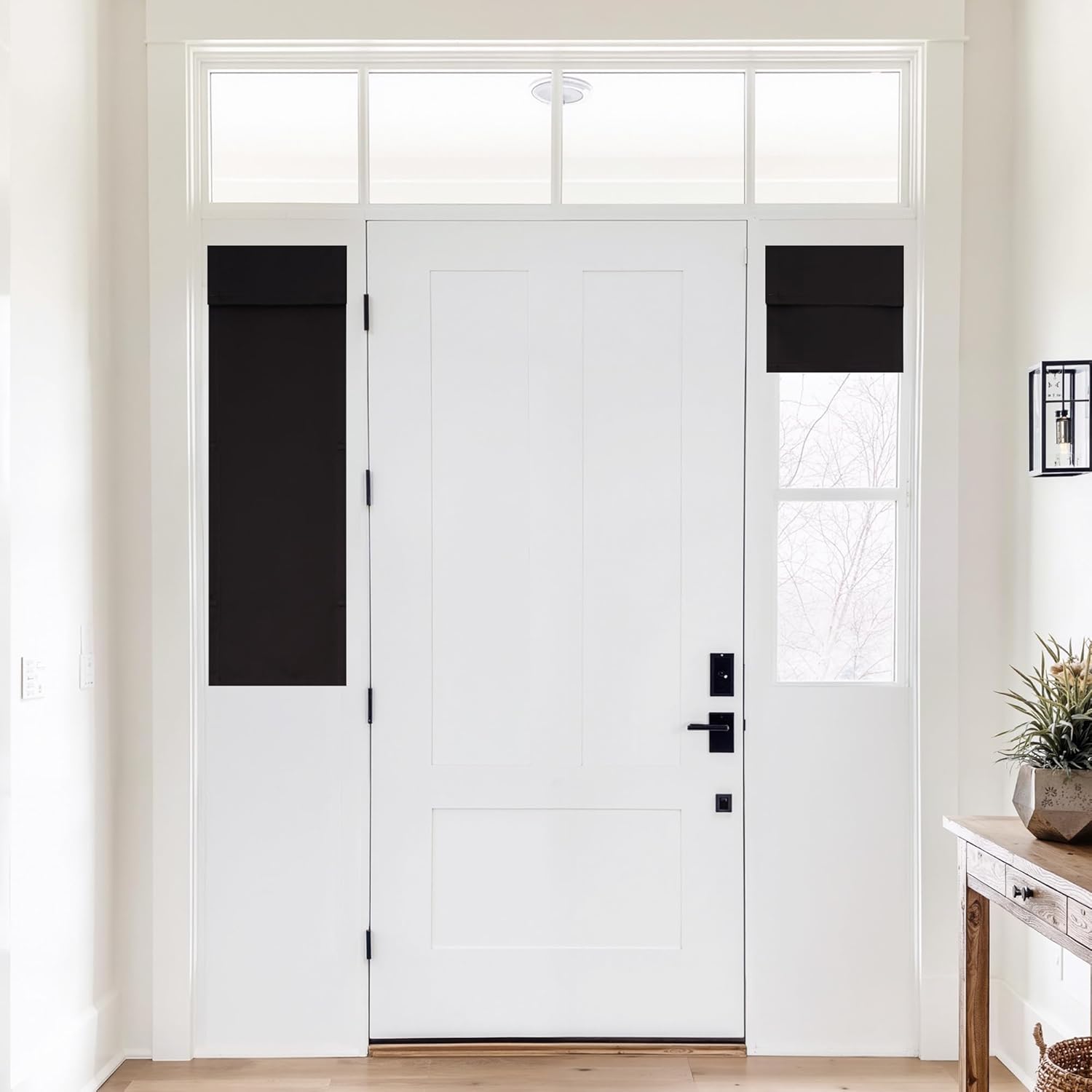Black blackout roman shades partially rolled on sidelight windows flanking a white entryway door.