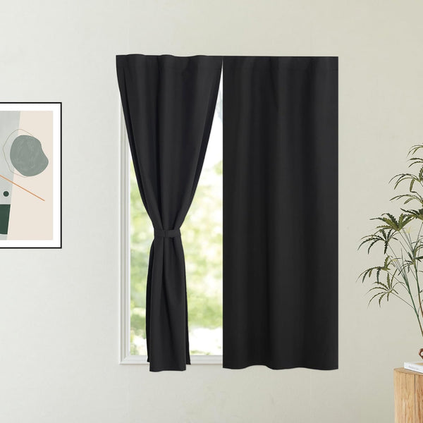 Pair of solid black blackout window curtains, one panel tied back, in a modern interior.