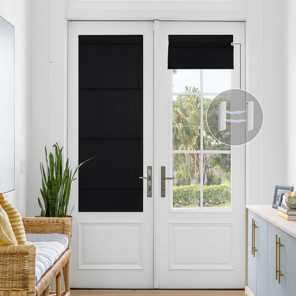 Black cordless magnetic blackout shades installed on white French door. One extended, other rolled, revealing tropical outdoor view.