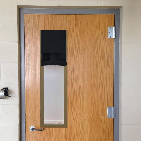 Black fabric privacy and blackout cover for a door window, partially rolled up and secured with straps on a light brown wooden door.
