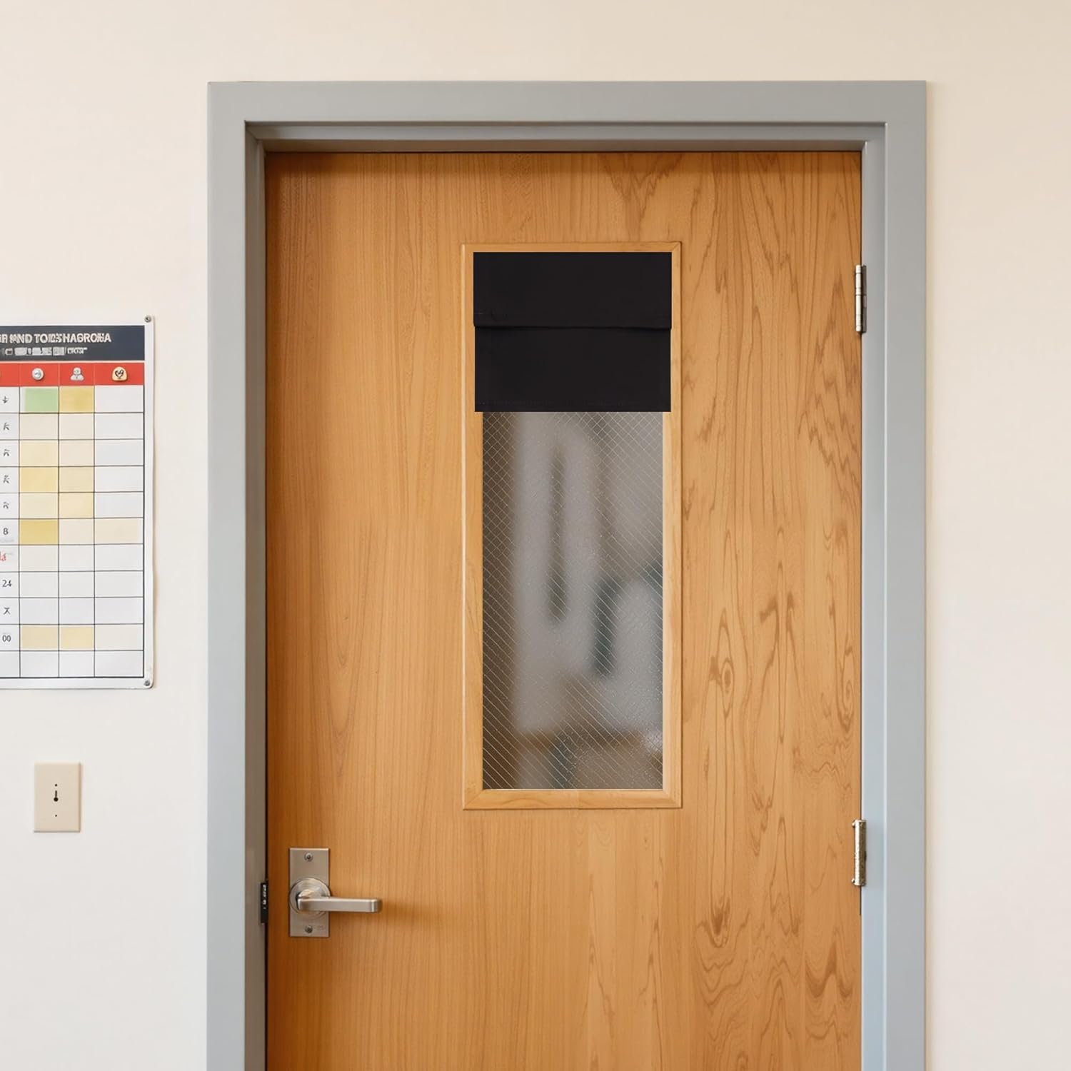 Black fabric privacy shade partially covers a textured glass door window on a light wood office door.