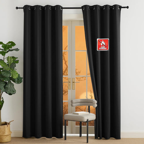Solid black flame retardant blackout curtains with silver grommets, hanging over a glass door.