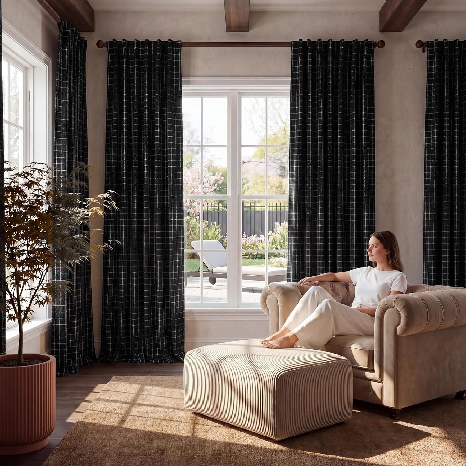 Black grid patterned curtains in a cozy modern living room with a woman relaxing in an armchair.