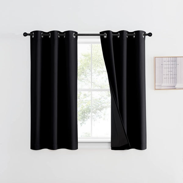 Pair of black grommet blackout curtains hanging on a rod above a window in a white room