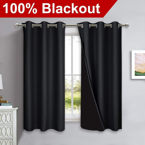 Pair of black blackout curtains with silver grommet tops hanging on a rod. One curtain slightly open.