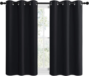 Pair of solid black blackout curtains with silver grommet tops on a window rod.