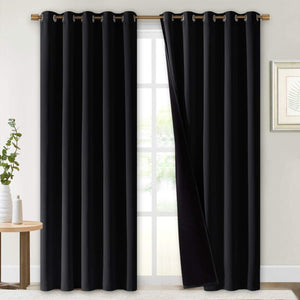 Pair of solid black blackout curtains with bronze grommet tops, hanging on a window rod.