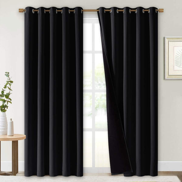Pair of solid black blackout curtains with bronze grommet tops, hanging on a window rod.