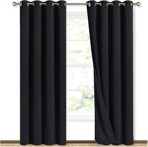 Pair of black blackout curtains with silver grommets hanging on a gold rod, partially open to a bright window.