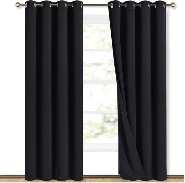 Pair of black blackout curtains with silver grommets hanging on a gold rod, partially open to a bright window.