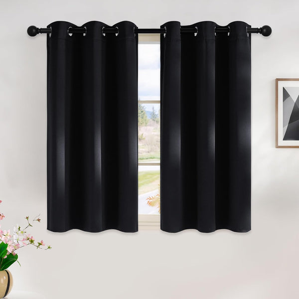 Two black blackout curtains with silver grommet tops hanging on a black rod over a window.