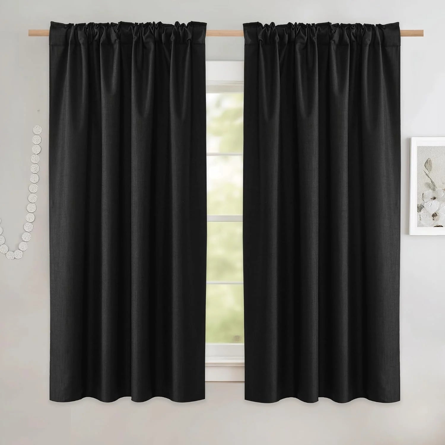Black linen-look rod pocket curtains hanging on a wooden pole over a bright window