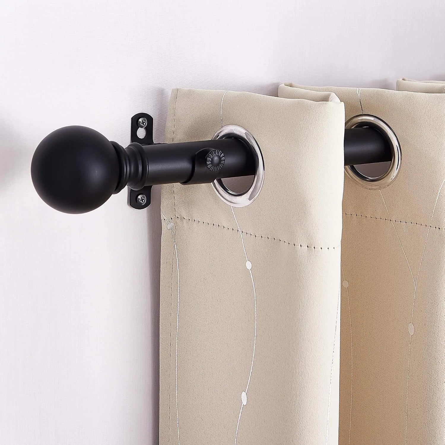 Black metal curtain rod with round finial holding beige grommet curtains