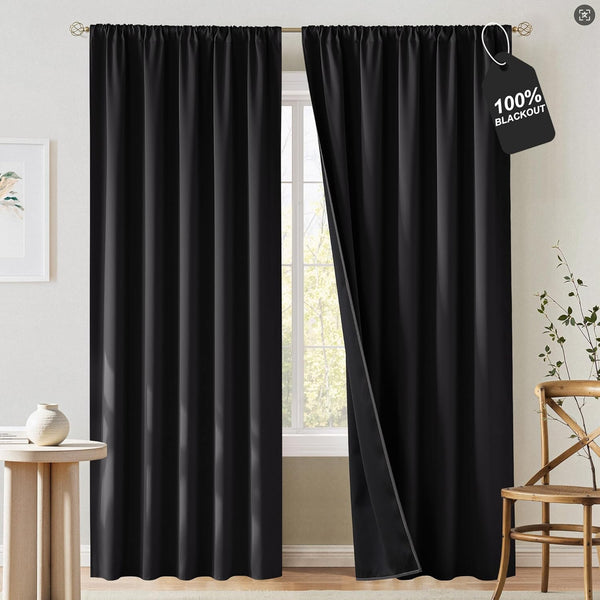 A pair of black rod pocket blackout curtains hanging on a gold rod over a window, one panel slightly open.