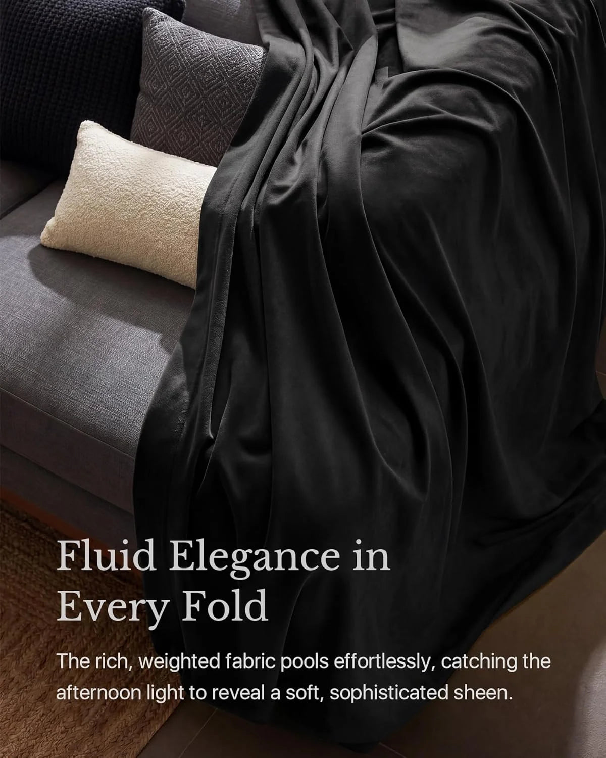Black weighted sateen throw blanket draped over a gray sofa with textured pillows