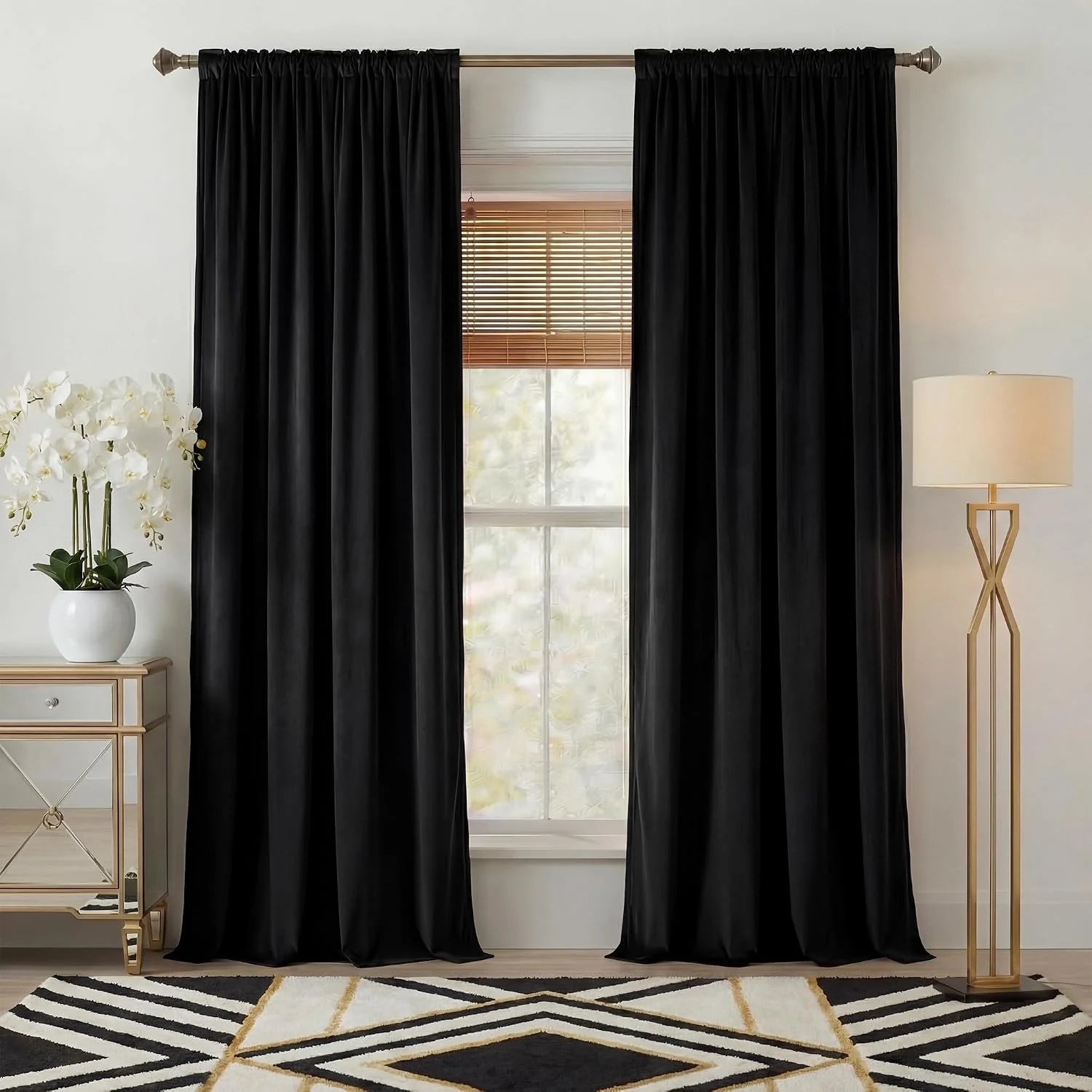 Black satin-look curtains on a bronze rod in a modern room with lamp and orchid