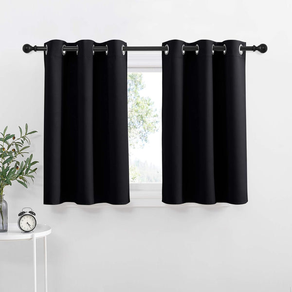 Black grommet top blackout curtains hung on a rod covering a window in a bright room.