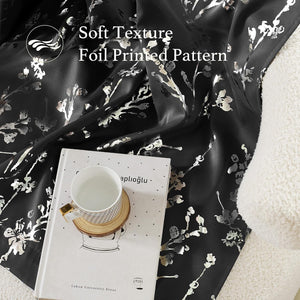 Soft black fabric with shimmering silver foil printed floral pattern, draped beside a book.