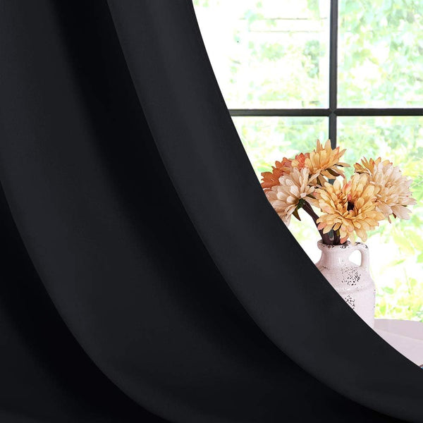 Smooth black solid curtain panel hanging, revealing a window and a vase of flowers.