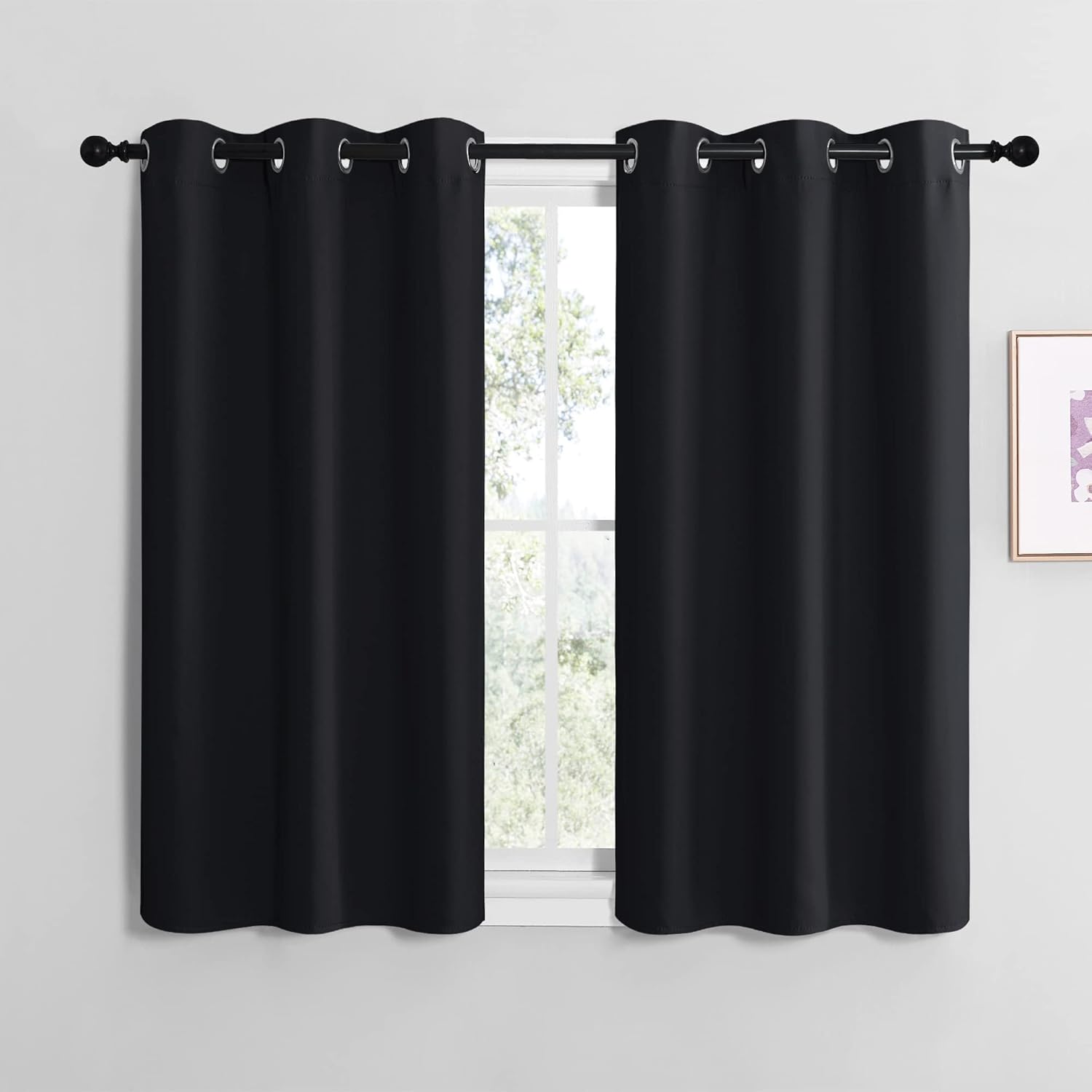 Pair of black solid smooth grommet top short curtains hanging on a dark rod over a window.