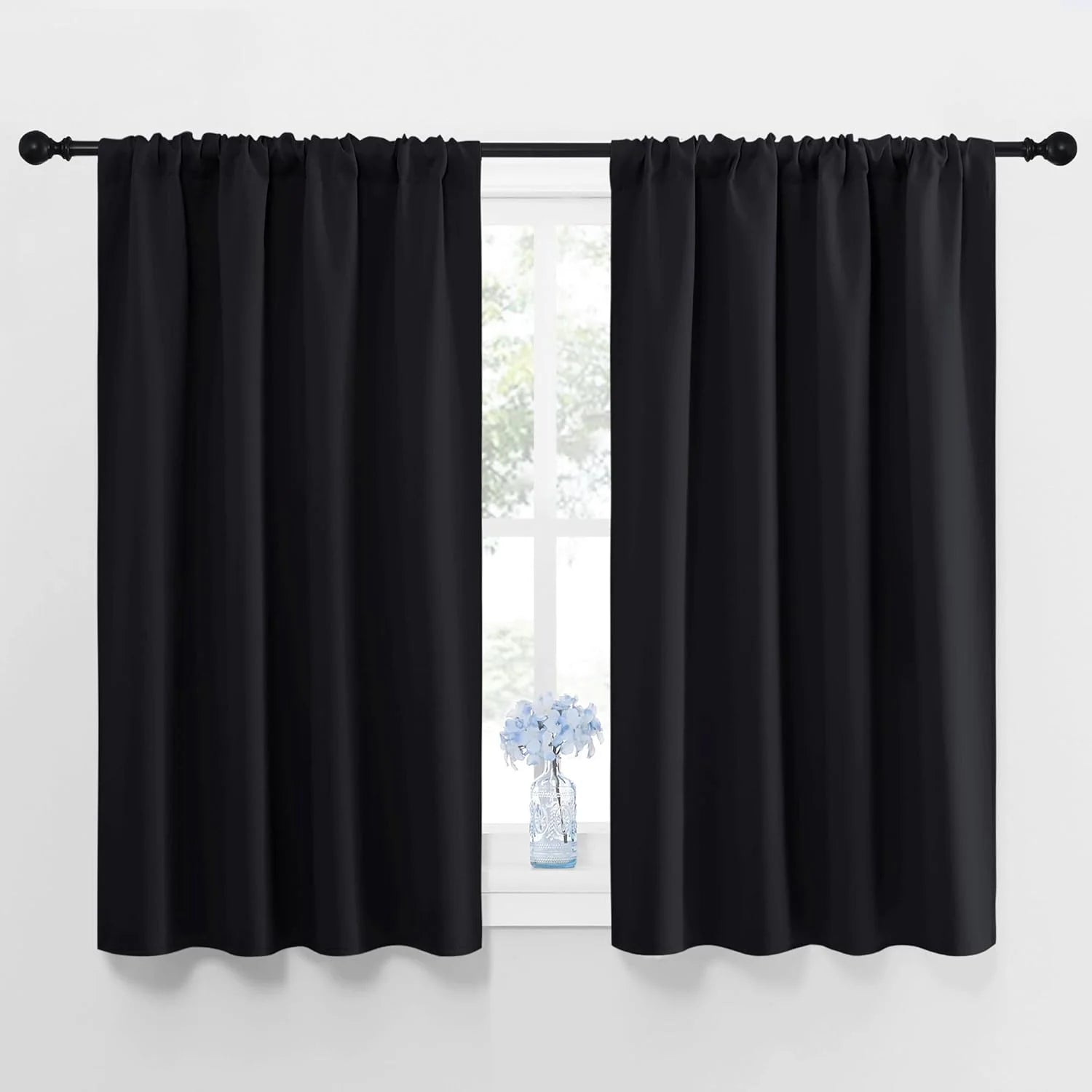 Pair of solid black rod pocket window curtains on a dark rod, bright window.