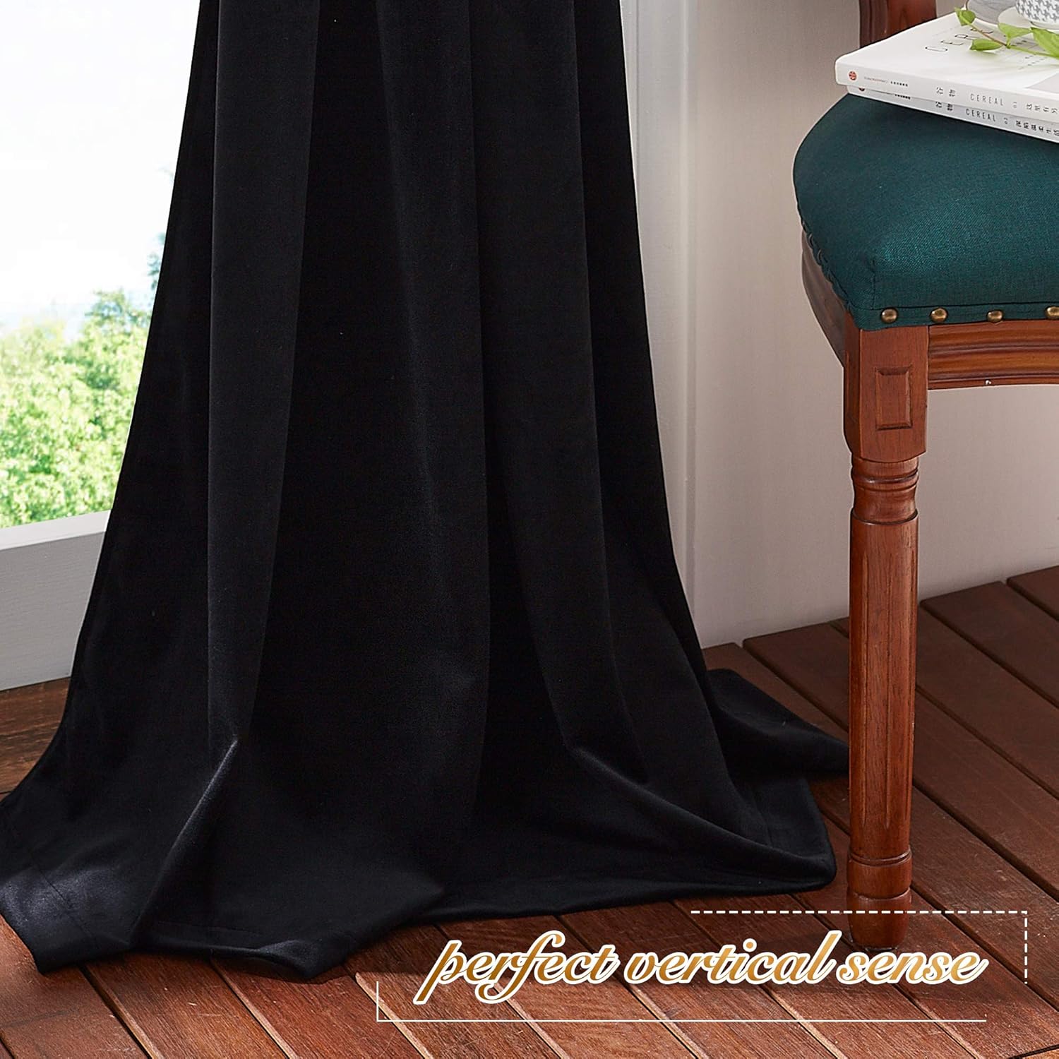 Black velvet blackout curtain hanging full length by a window, pooling on wooden floor, with green trees visible outside.
