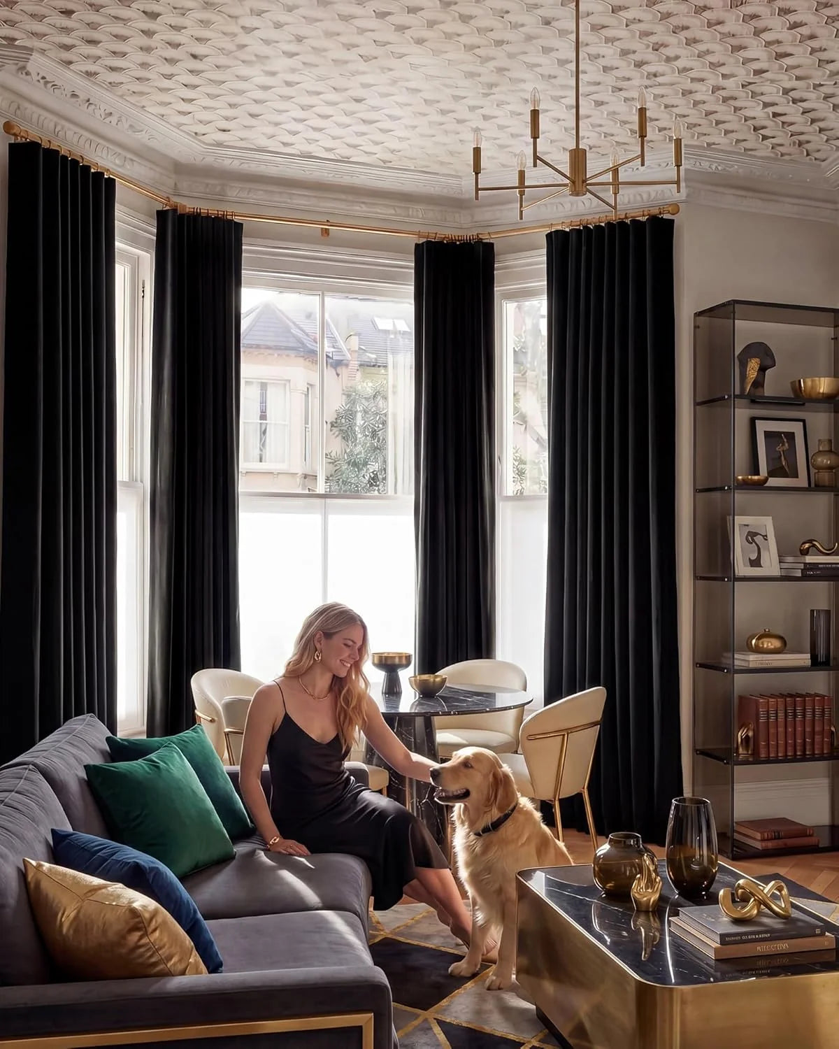 Black velvet curtains in an elegant living room with brass accents, sofa, woman, and dog