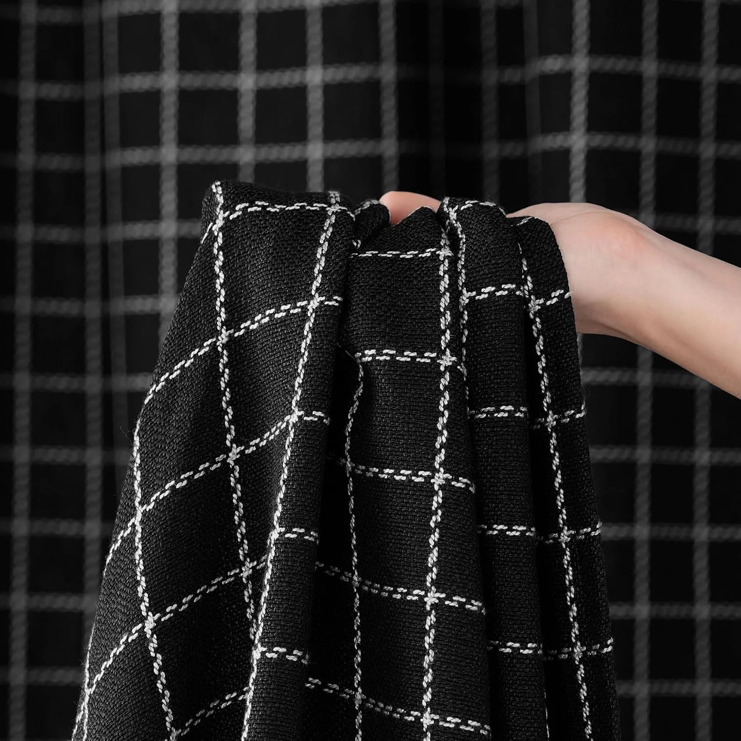 Hand holding black woven fabric with white windowpane plaid pattern