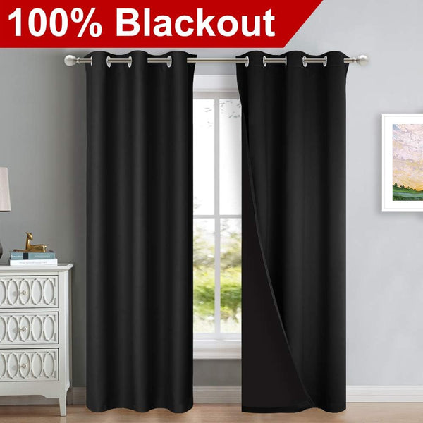 Black blackout curtains with silver grommet tops hang on a rod. One panel is slightly open, showing thick fabric.