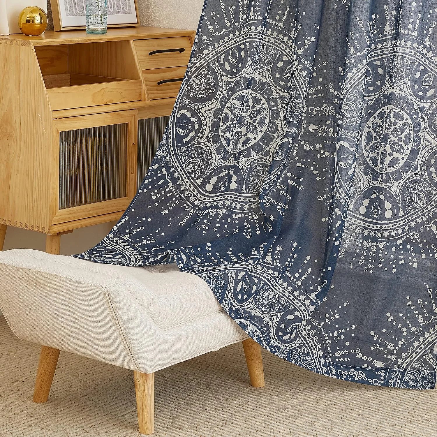 Blue sheer curtain with white boho medallion print draped beside a wooden cabinet