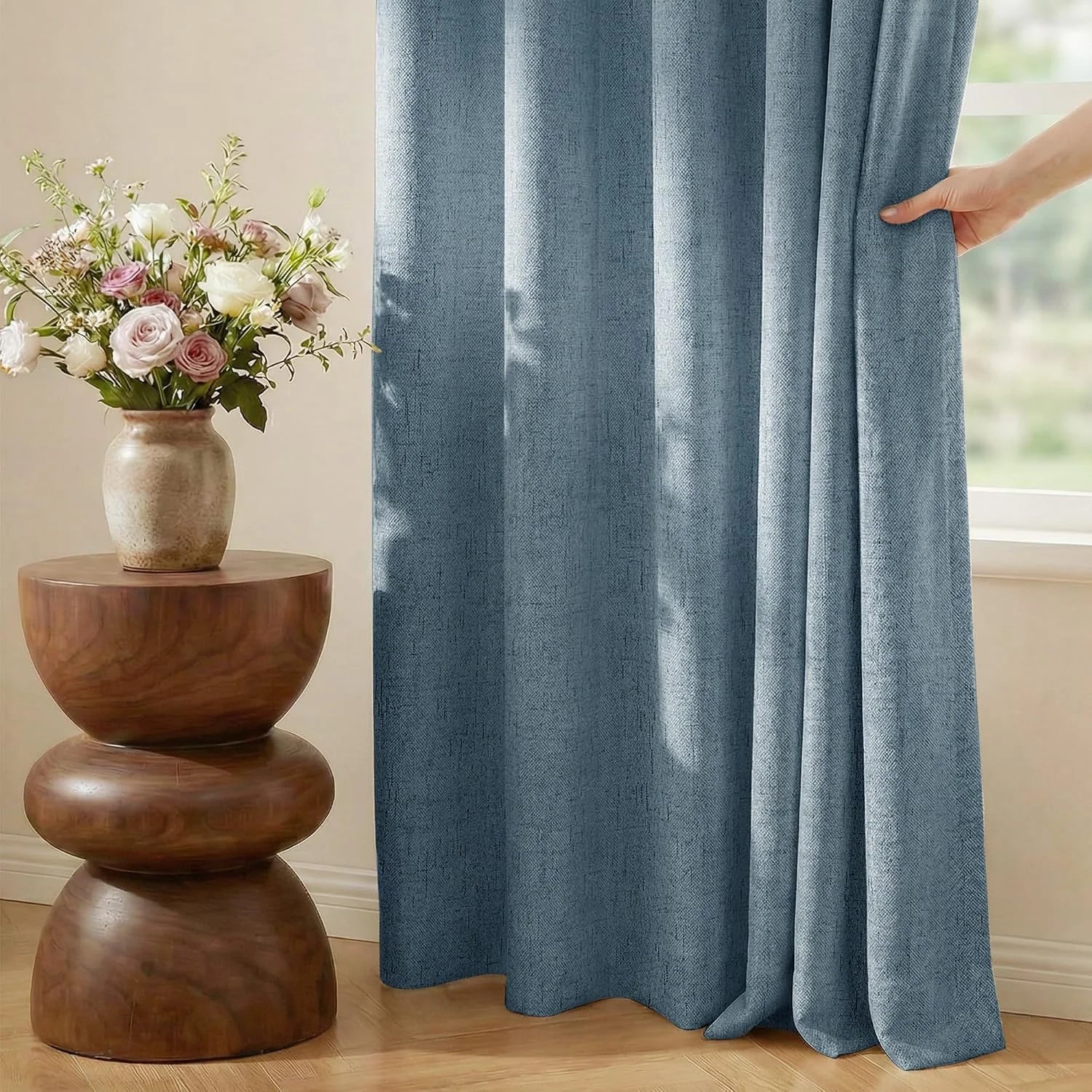 Textured blue linen-look curtain beside a window with a wooden side table and flowers
