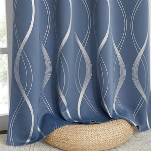 Blue blackout curtain panel with metallic silver geometric wave pattern, pooling on a woven pouf by a window.