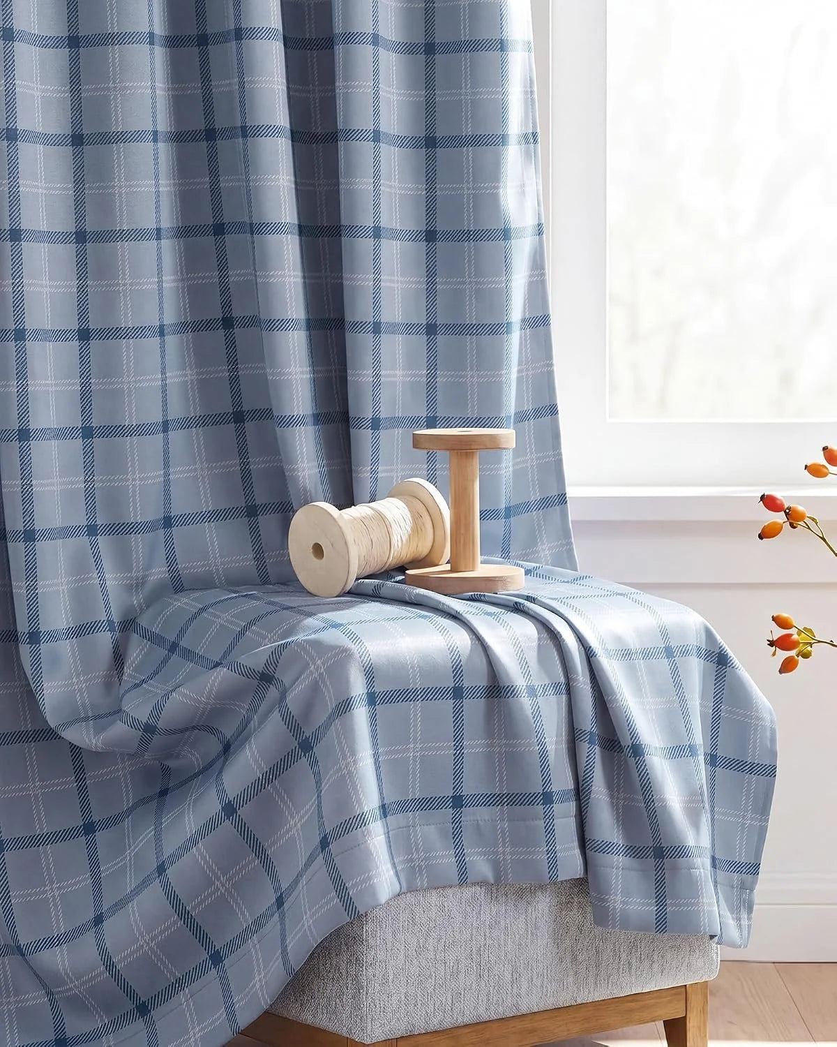 Blue plaid fabric draped over a bench beside a bright window with wooden spools