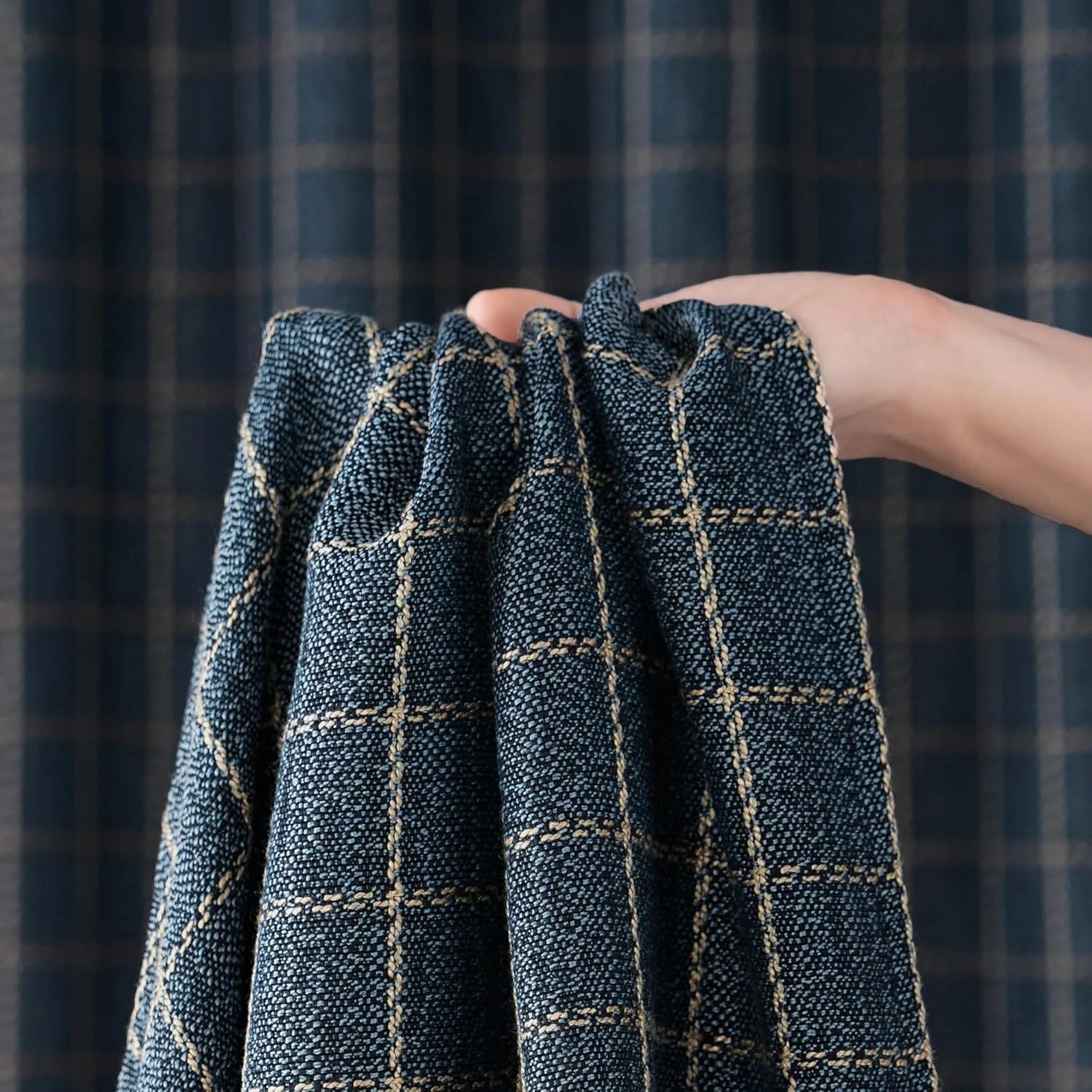 Hand holding dark blue plaid textured curtain fabric, showcasing woven pattern and detailed weave