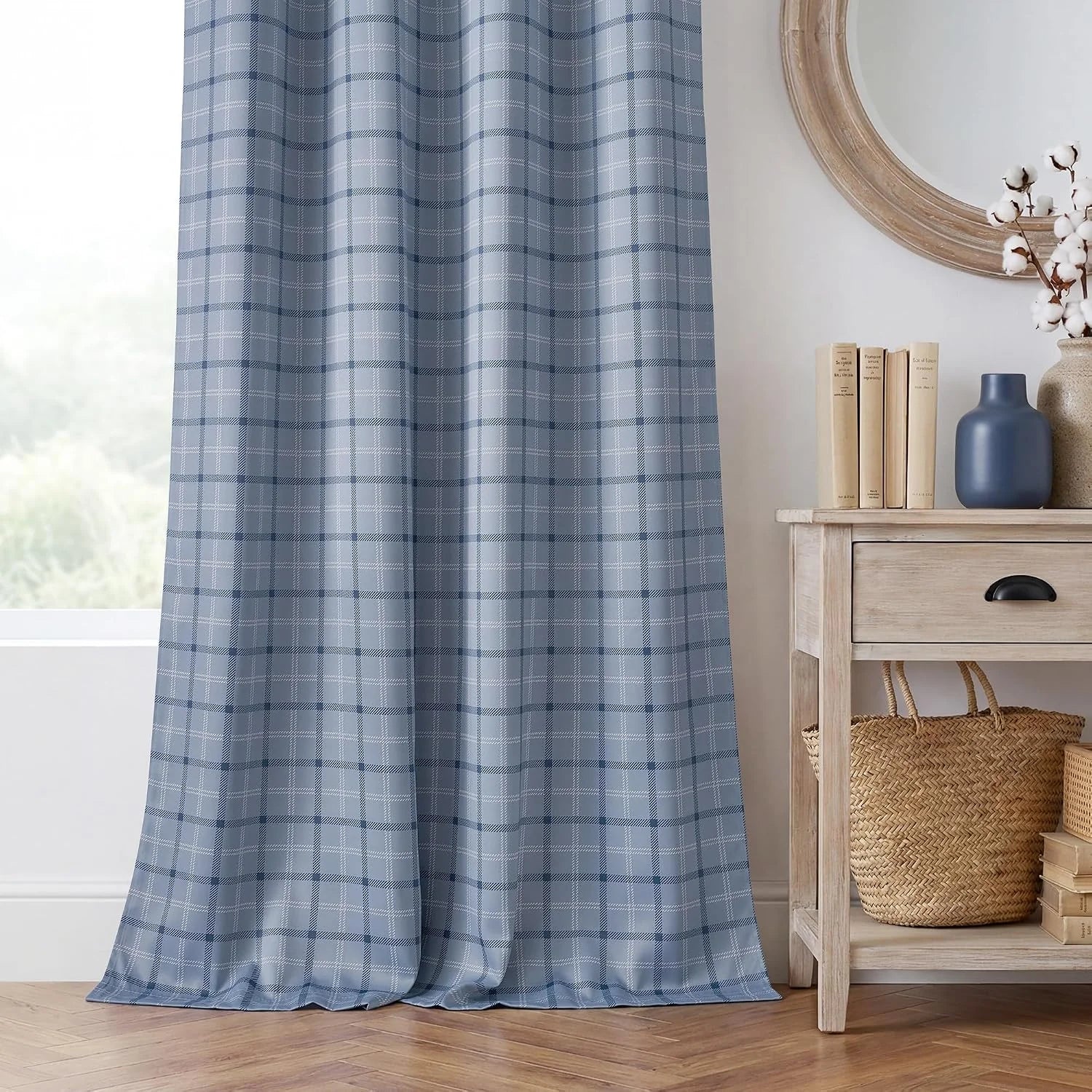 Blue plaid curtain panel hanging in a bright room beside a light wood console table