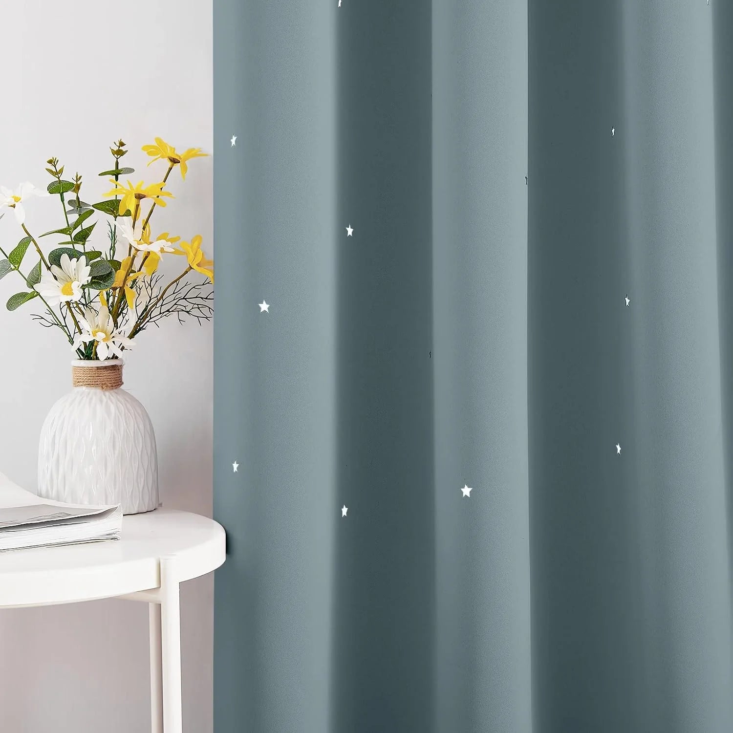 Dusty blue curtain panel with small white stars beside a white side table and vase