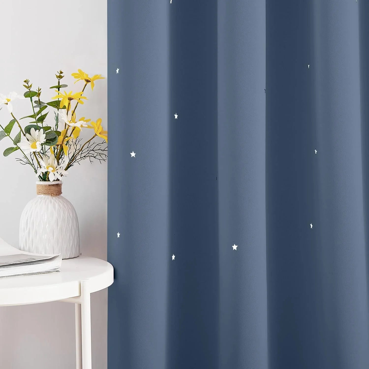 Blue blackout curtain with small white star print beside a white table and flower vase