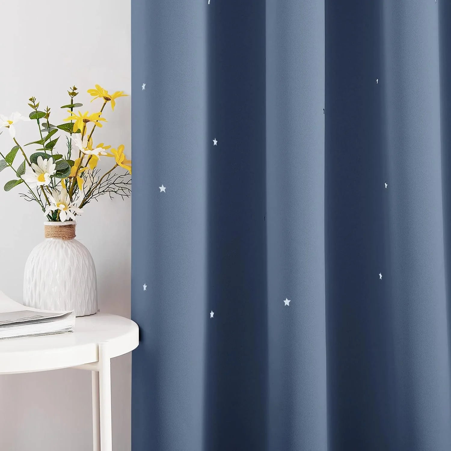 Blue blackout curtain with small white star print beside a white table and vase