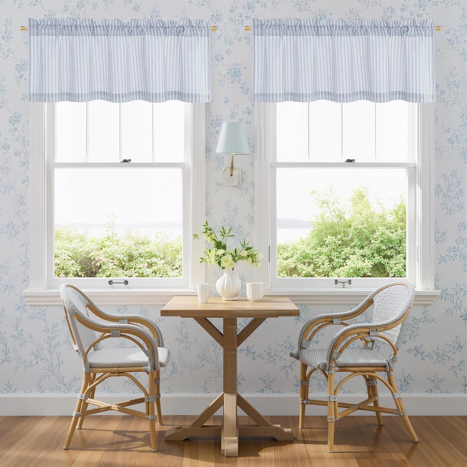 Two blue and white striped gathered valance curtains on gold rods above windows in a room with floral wallpaper.