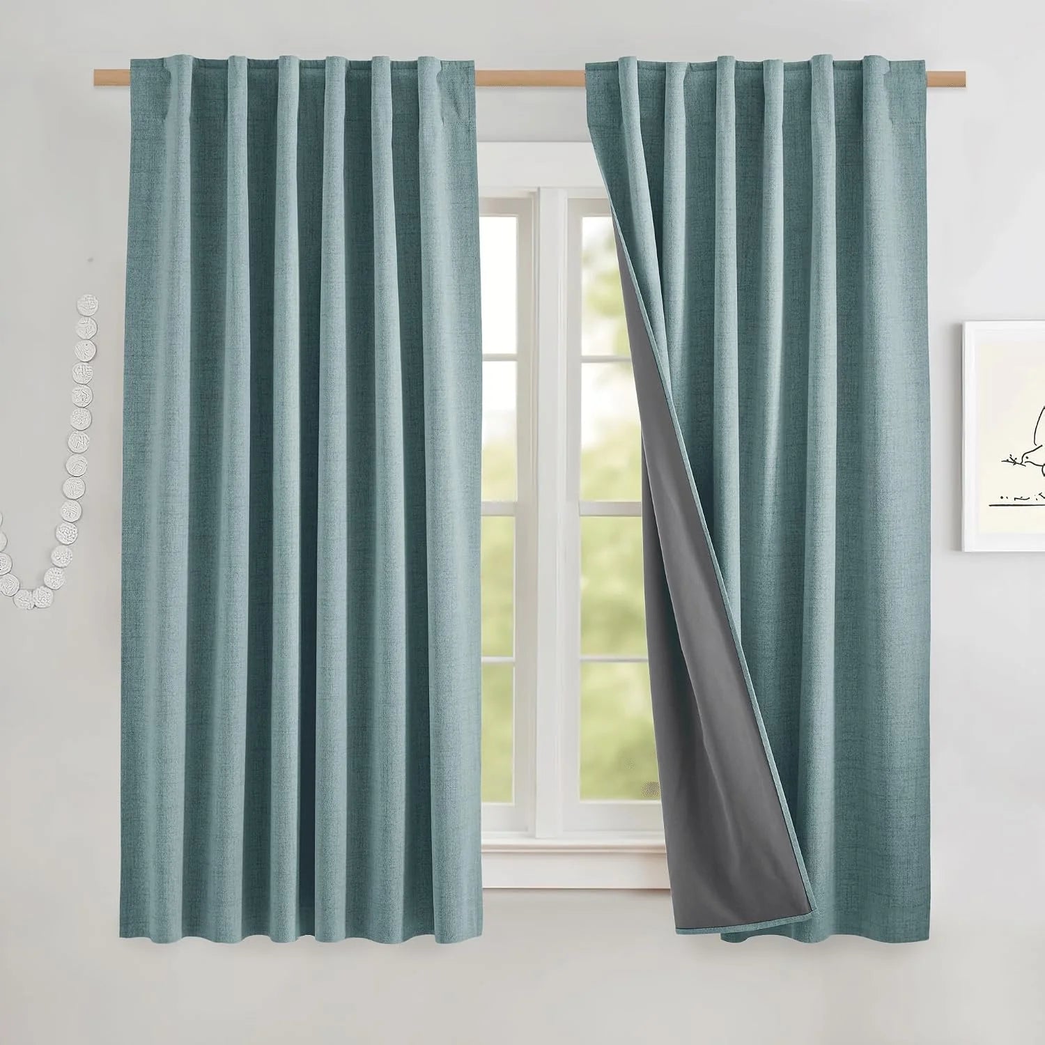 Light blue textured blackout curtain panels on a wood rod, one panel pulled back to show gray lining