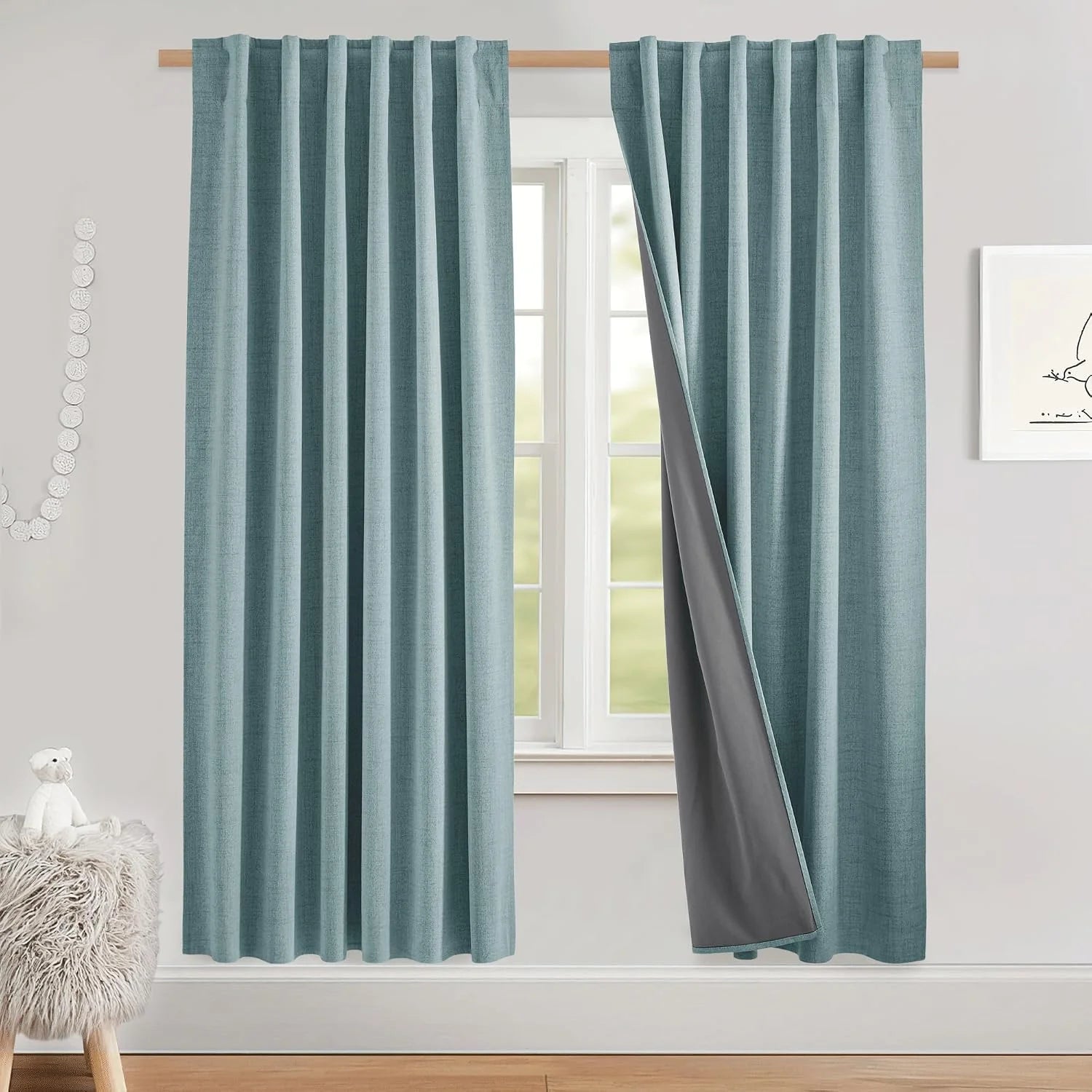 Light blue textured blackout curtains on a wooden rod, one panel pulled back to show gray lining