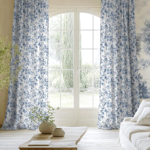 White curtains with blue floral toile pattern hanging elegantly by an arched living room window.