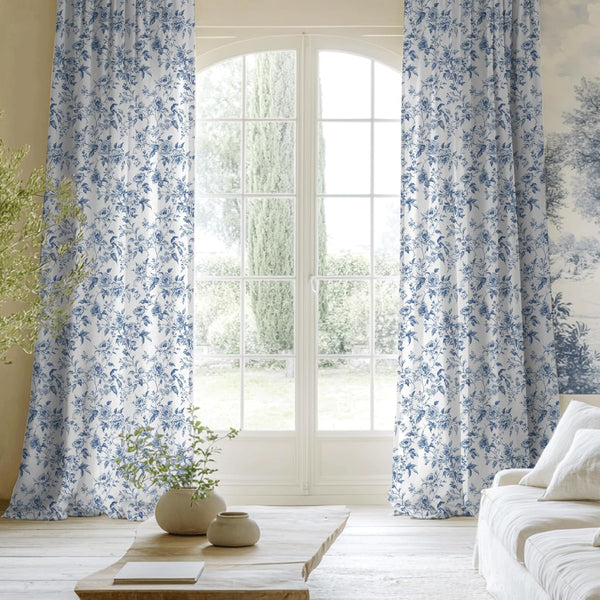 White curtains with blue floral toile pattern hanging elegantly by an arched living room window.