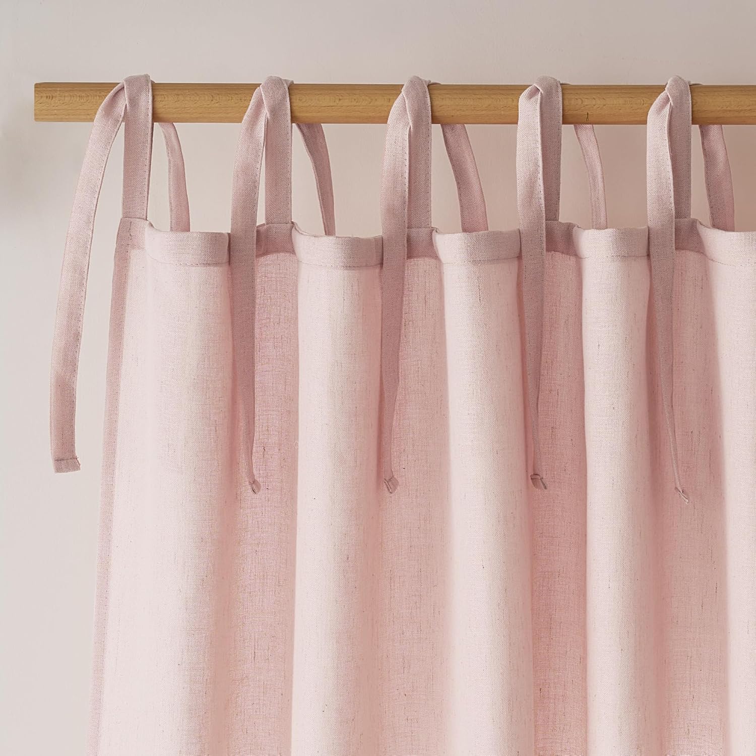 Blush pink linen curtain panel with visible tie-top tabs, hanging on a rustic wooden rod.