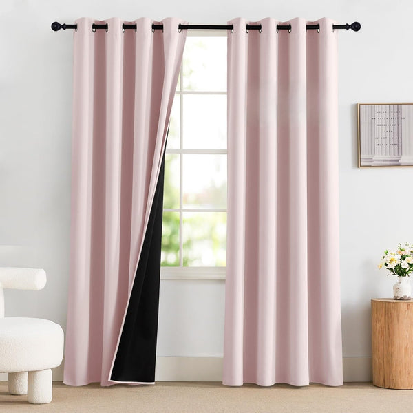 Blush pink blackout curtains with black lining and grommet top, hanging on a black rod in a bright room.
