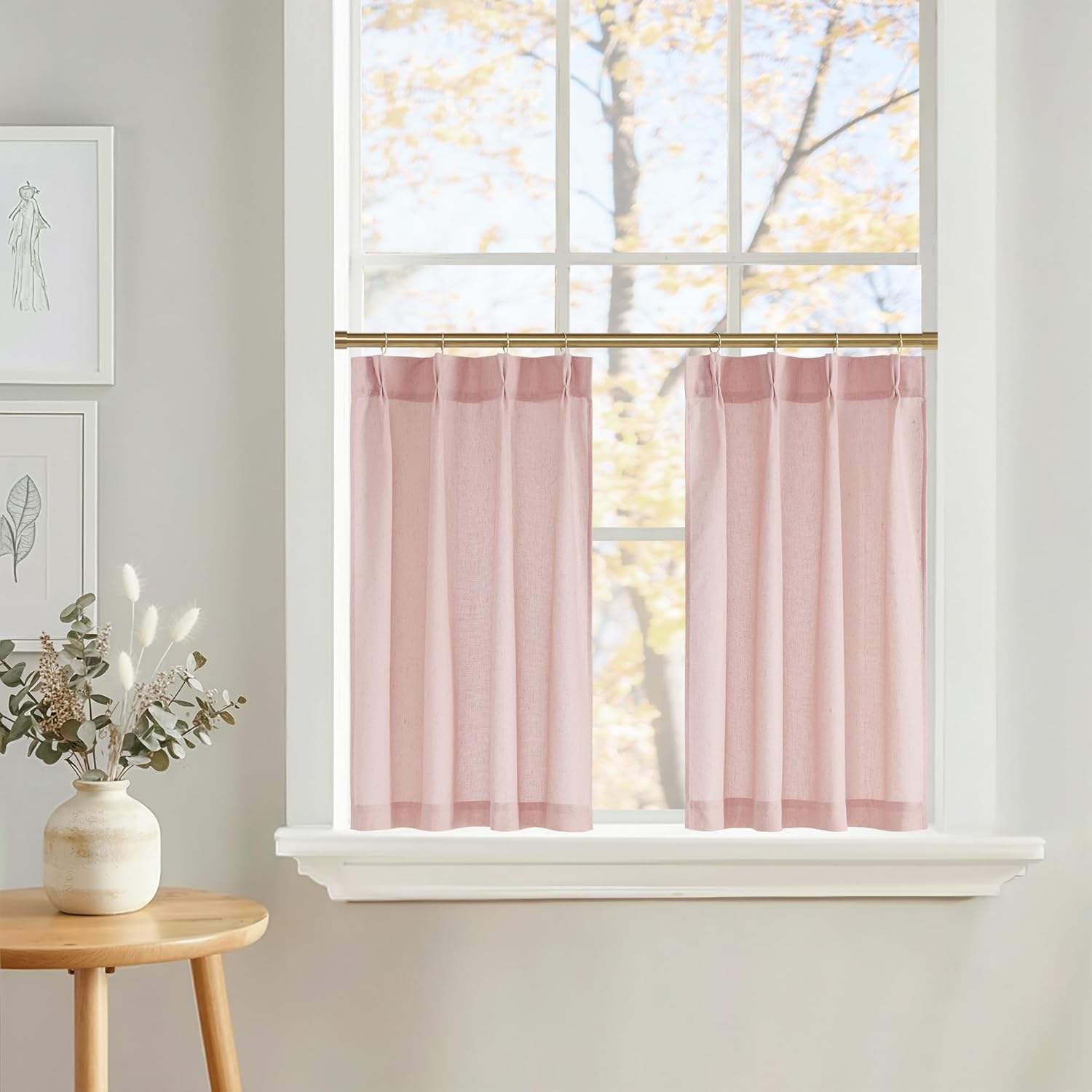 Pair of blush pink linen blend cafe curtains with a rod pocket top hanging from a brass rod on a sunlit window.