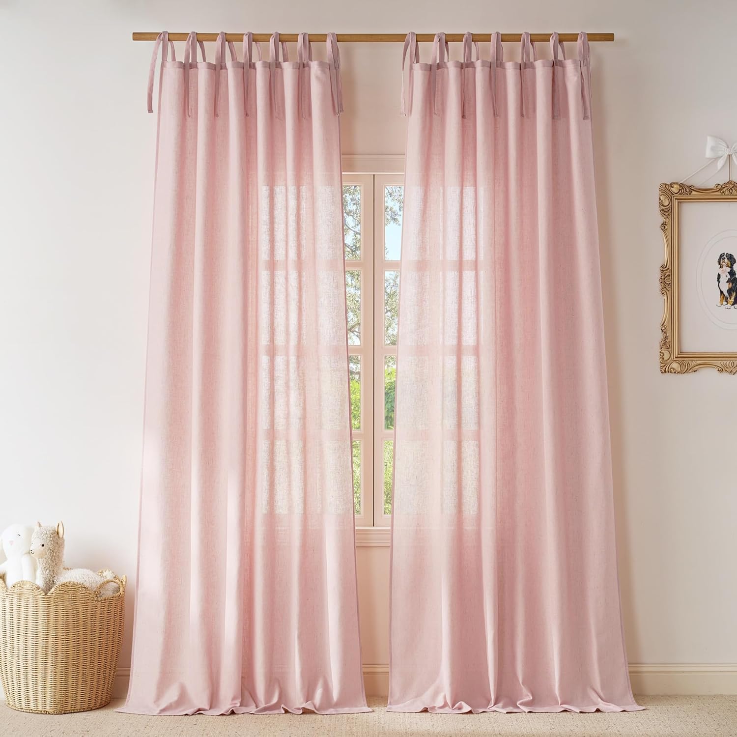 Two blush pink linen tie-top sheer curtains hang on a wooden rod, filtering light into a bright room.